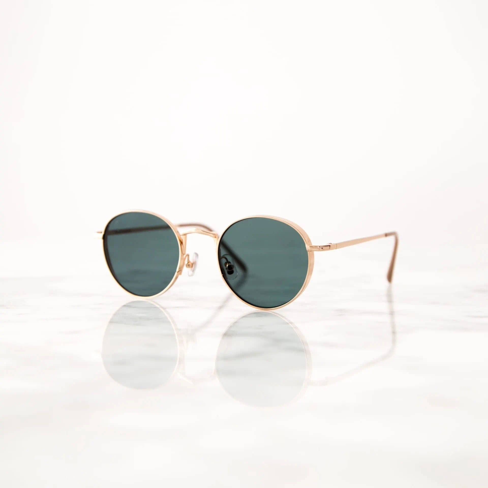 Lunettes de soleil à monture dorée sur surface réfléchissante en marbre